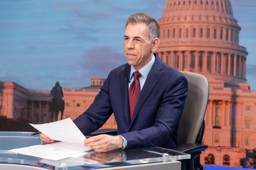 Mark Albert at a television news desk with the U.S. Capitol behind him